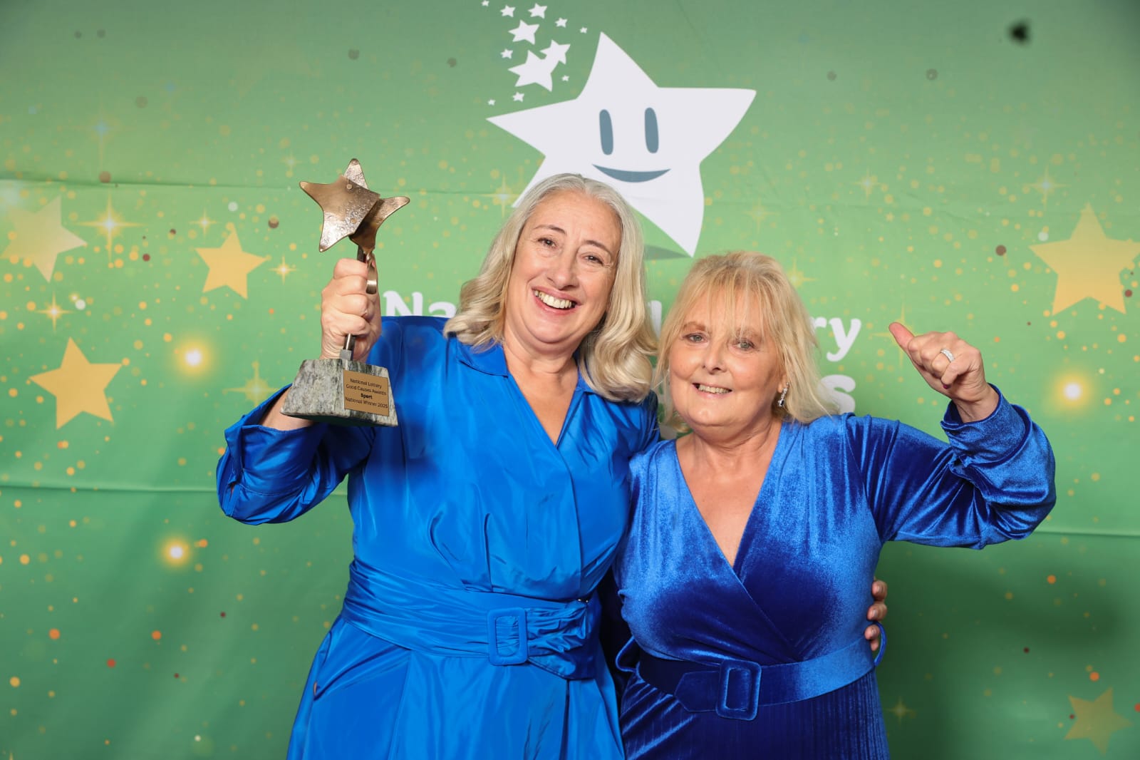 Denise and Michelle dressed in blue dresses, celebrating with the award.